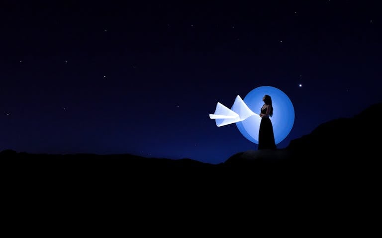 Captivating silhouette of a woman under the stars with creative light painting against a deep blue night sky.